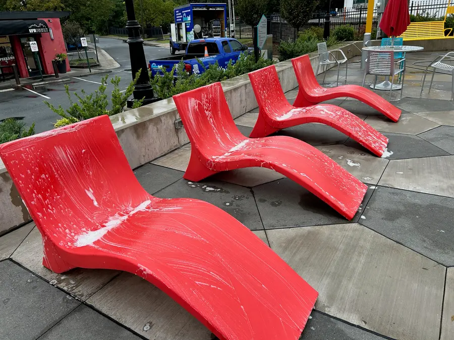Red plastic lounge chairs covered in soap suds during an outdoor furniture wash, action shot.